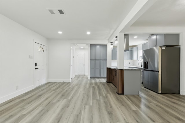 kitchen featuring visible vents, a sink, stainless steel fridge, light wood-style floors, and decorative backsplash