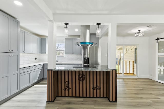 kitchen with gray cabinetry, stainless steel fridge, light wood-style floors, tasteful backsplash, and island range hood