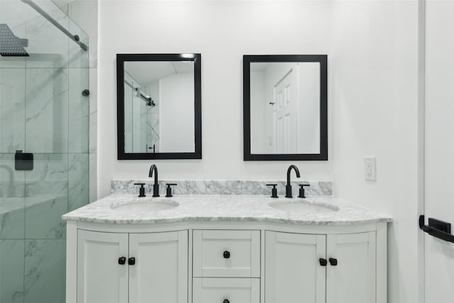 full bath with double vanity, a marble finish shower, and a sink