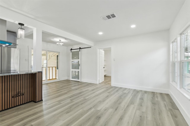 empty room with a barn door, light wood-style flooring, visible vents, and a wealth of natural light