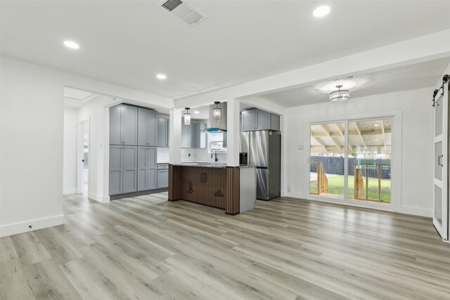 kitchen featuring visible vents, gray cabinetry, open floor plan, a barn door, and stainless steel fridge