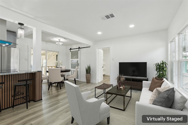 living area with visible vents, baseboards, a barn door, recessed lighting, and light wood-style floors