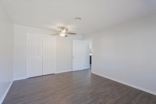 unfurnished bedroom featuring baseboards, dark wood-style flooring, a closet, and ceiling fan