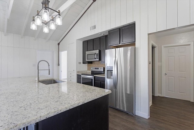 kitchen featuring light stone counters, dark wood finished floors, beam ceiling, a sink, and appliances with stainless steel finishes