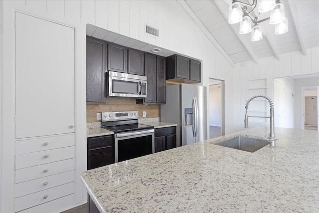 kitchen featuring visible vents, lofted ceiling with beams, light stone counters, appliances with stainless steel finishes, and a sink