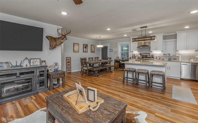 living area with recessed lighting, light wood-style flooring, ornamental molding, and ceiling fan