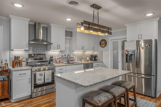 kitchen with visible vents, ornamental molding, a sink, appliances with stainless steel finishes, and wall chimney exhaust hood