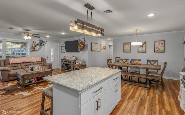 kitchen featuring visible vents, light wood-style flooring, white cabinetry, crown molding, and a center island