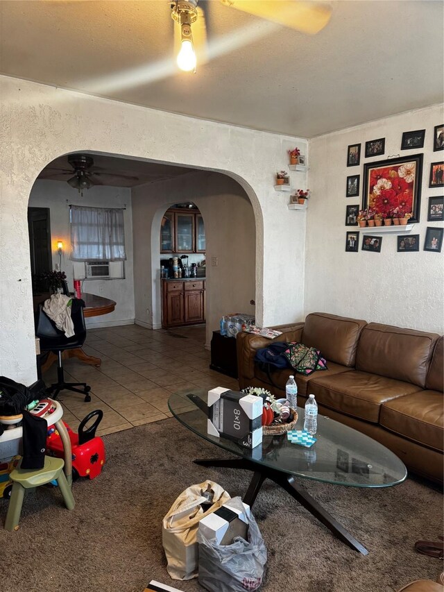 carpeted living area featuring arched walkways, tile patterned floors, ceiling fan, and a textured wall