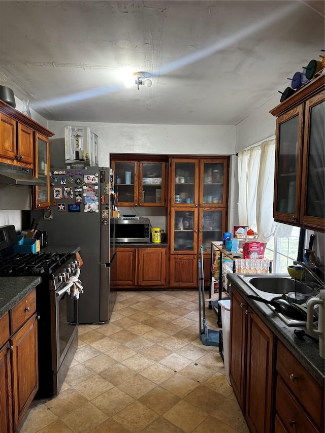 kitchen featuring under cabinet range hood, a sink, dark countertops, stainless steel appliances, and brown cabinetry