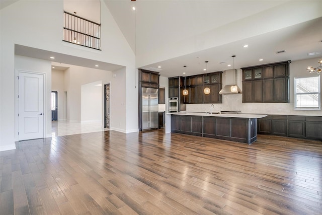 kitchen with stainless steel built in refrigerator, dark brown cabinetry, wall chimney exhaust hood, and wood finished floors