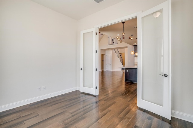 empty room featuring visible vents, baseboards, dark wood finished floors, a chandelier, and stairs