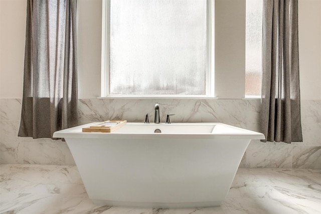 bathroom featuring marble finish floor and a freestanding bath