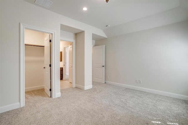 unfurnished bedroom featuring a walk in closet, baseboards, visible vents, and light carpet