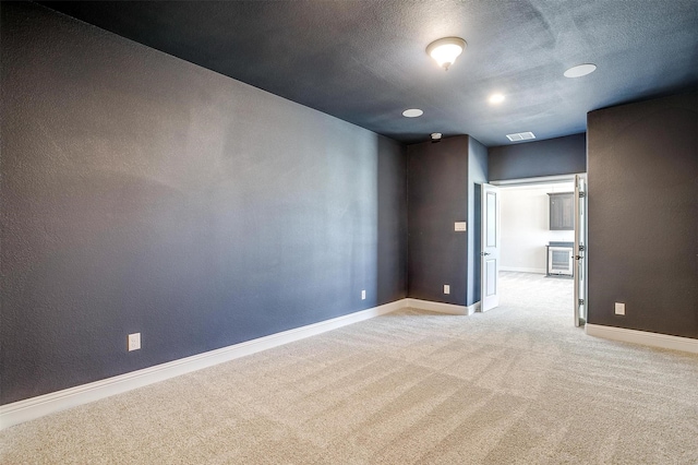 spare room with visible vents, light colored carpet, a textured ceiling, and baseboards