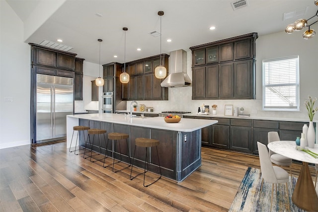 kitchen featuring visible vents, appliances with stainless steel finishes, light countertops, and wall chimney range hood