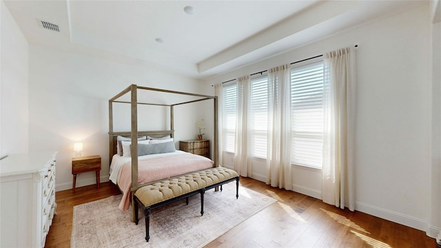 bedroom with a tray ceiling, visible vents, light wood-type flooring, and baseboards