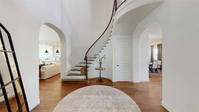 stairway featuring arched walkways, baseboards, a towering ceiling, and wood finished floors