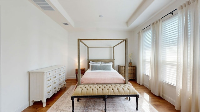 bedroom featuring a tray ceiling, visible vents, light wood-type flooring, and baseboards