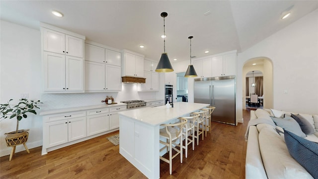 kitchen with arched walkways, stainless steel appliances, light countertops, light wood-style floors, and open floor plan