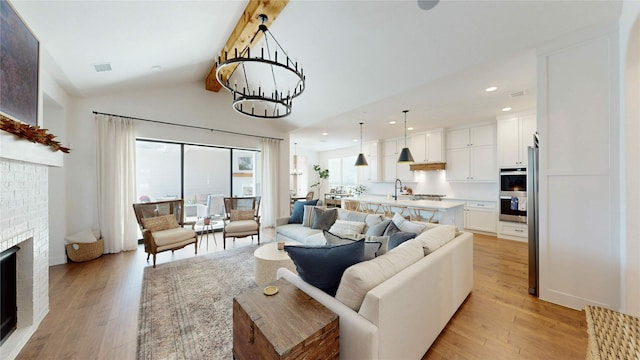 living room featuring light wood finished floors, a chandelier, a brick fireplace, and lofted ceiling with beams