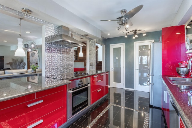 kitchen with red cabinetry, dark tile patterned flooring, a sink, appliances with stainless steel finishes, and wall chimney exhaust hood