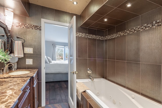 ensuite bathroom with vanity, wood finished floors, ensuite bathroom, tile walls, and a jetted tub