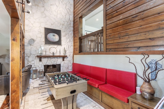 recreation room with a stone fireplace and wood walls