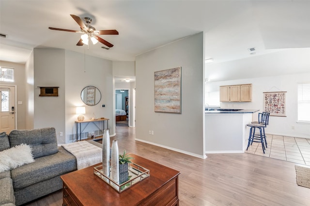 living area with baseboards, visible vents, a ceiling fan, and light wood-style floors