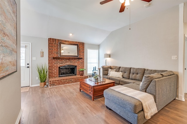 living room featuring a wealth of natural light, lofted ceiling, a brick fireplace, and wood finished floors