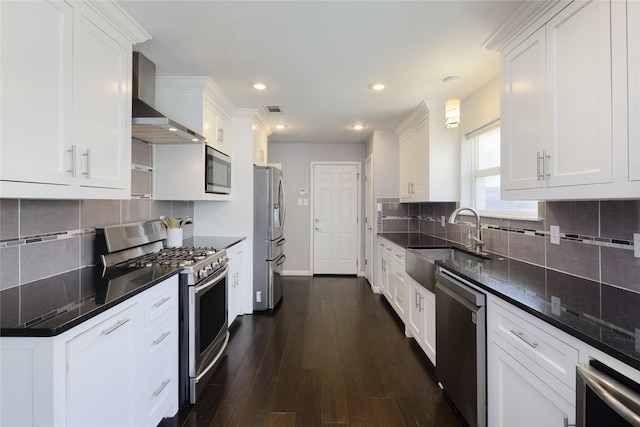 kitchen with visible vents, a sink, appliances with stainless steel finishes, white cabinets, and wall chimney range hood