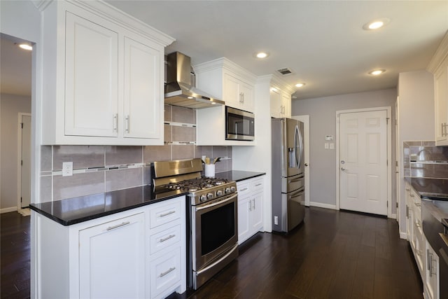 kitchen featuring dark countertops, white cabinets, appliances with stainless steel finishes, and wall chimney range hood