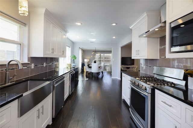 kitchen with a sink, white cabinetry, stainless steel appliances, wall chimney exhaust hood, and dark wood-style flooring