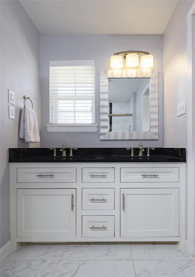 bathroom with double vanity, marble finish floor, walk in shower, and a sink