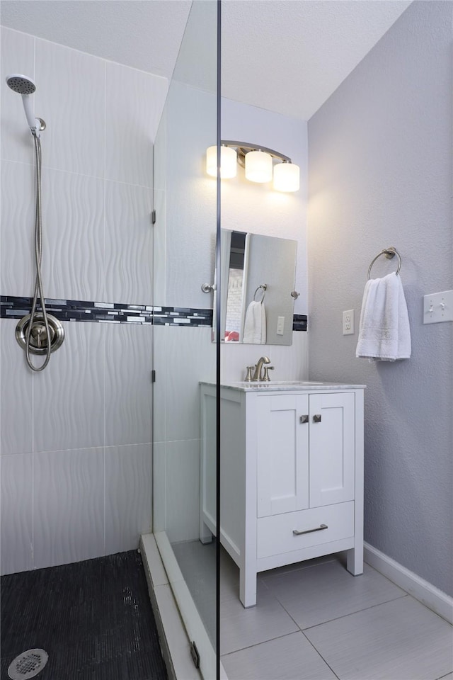 bathroom featuring vanity, tile patterned floors, baseboards, and tiled shower