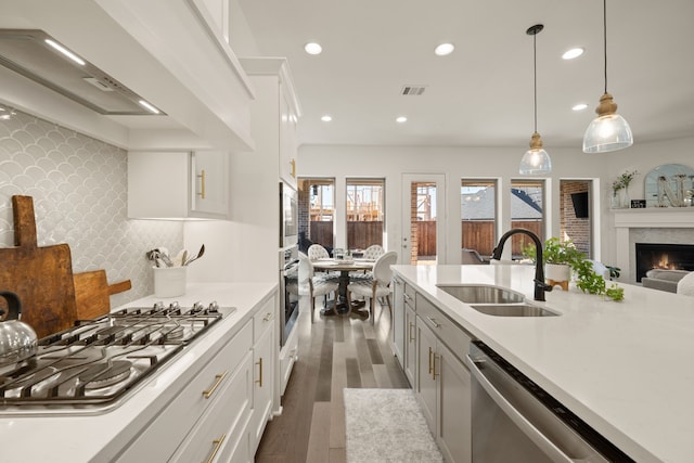 kitchen featuring visible vents, stainless steel appliances, a sink, light countertops, and wall chimney range hood