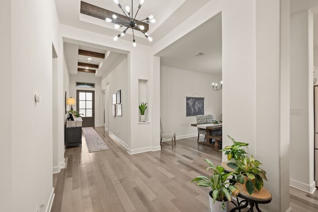 hall featuring visible vents, baseboards, a notable chandelier, and wood finished floors