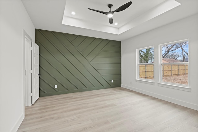 unfurnished room featuring an accent wall, a tray ceiling, a ceiling fan, and light wood-type flooring