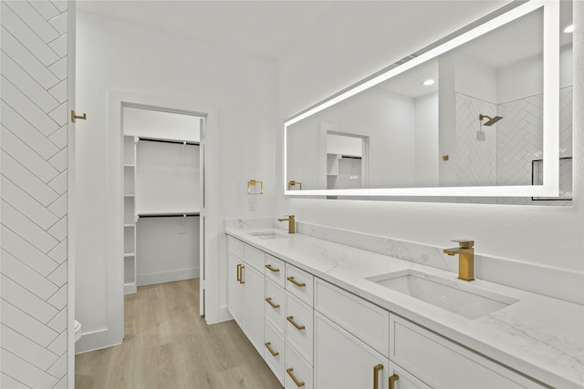 bathroom featuring a sink, tiled shower, wood finished floors, and double vanity