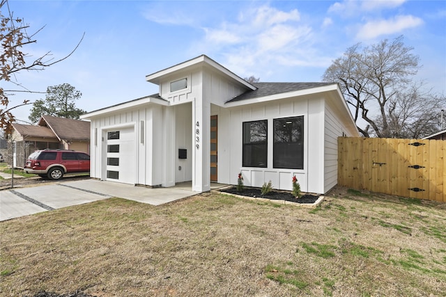 view of front of home featuring a front yard, fence, driveway, roof with shingles, and board and batten siding