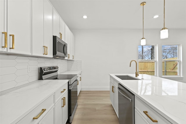 kitchen featuring decorative light fixtures, decorative backsplash, stainless steel appliances, white cabinetry, and a sink