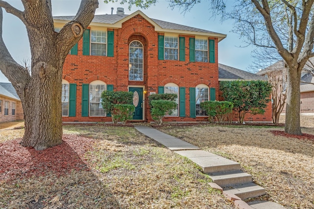 colonial-style house with a front lawn, brick siding, and roof with shingles