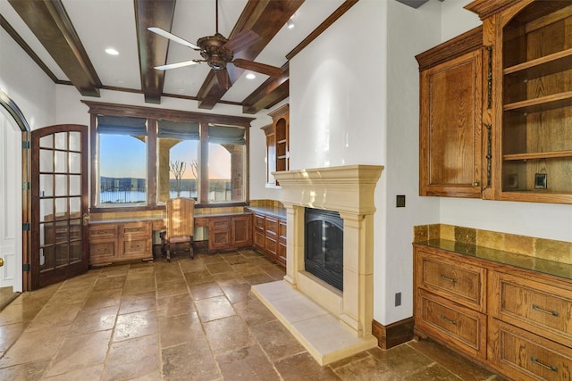 interior space with beamed ceiling, brown cabinets, a ceiling fan, stone tile flooring, and built in study area