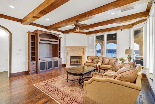 living area with visible vents, a fireplace with raised hearth, wood finished floors, arched walkways, and baseboards