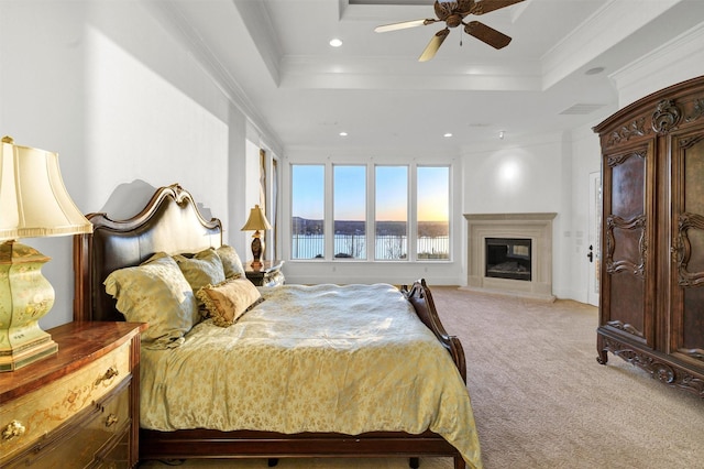 bedroom featuring recessed lighting, ornamental molding, light carpet, a glass covered fireplace, and a raised ceiling