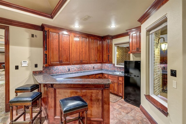 kitchen with visible vents, crown molding, a peninsula, freestanding refrigerator, and a sink