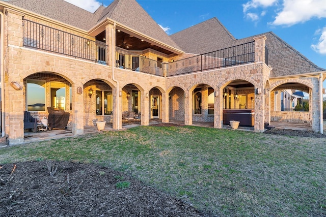 rear view of property featuring a hot tub, a shingled roof, a lawn, and a patio