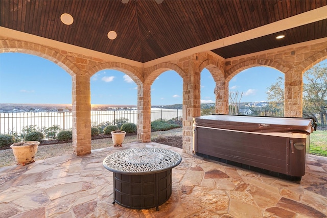 view of patio / terrace with fence, a water view, and a hot tub