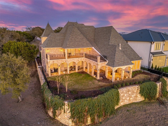 back of property featuring stone siding, fence, roof with shingles, a balcony, and a patio area