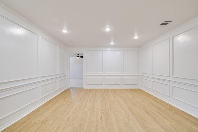 below grade area with a decorative wall, a ceiling fan, visible vents, and light wood finished floors